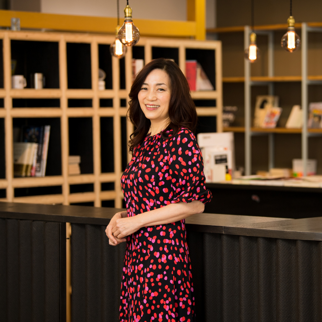 Photo de portait de Motoko Imada, femme influente dans la publicité, se tenant devant un comptoir avec des étagères en fond
